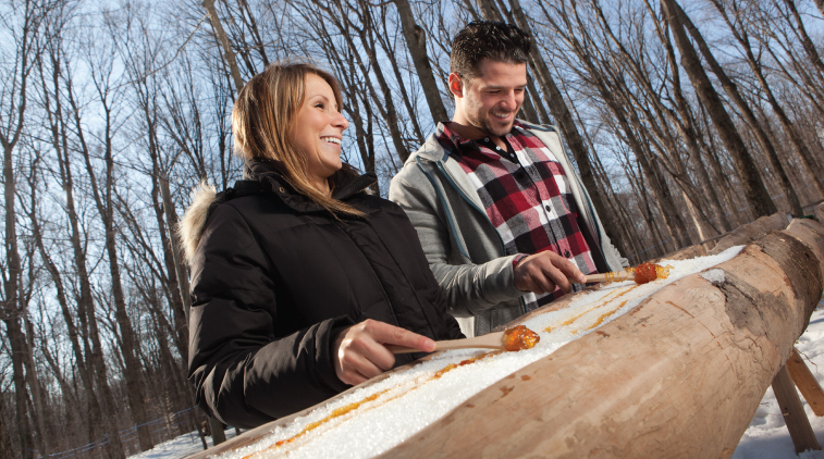 A woman and a man making maple taffy on snow